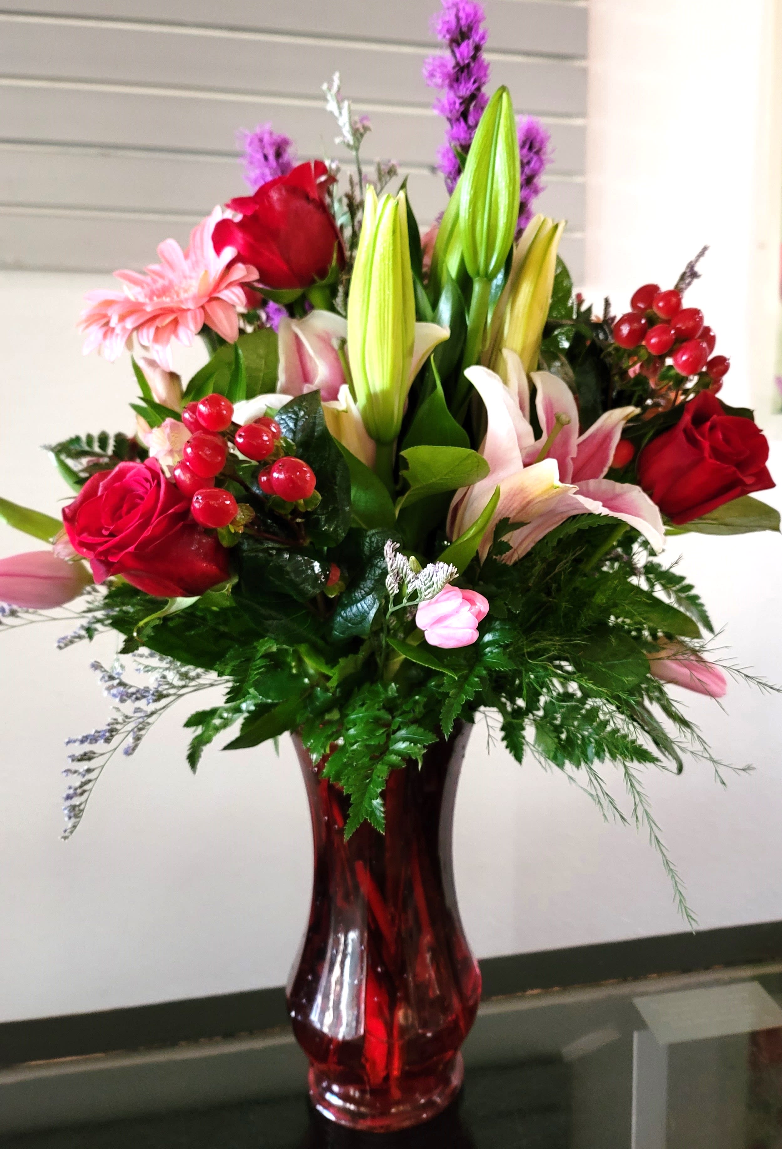 Mixed bouquet of lilies, roses, and pink daisies in a red glass vase