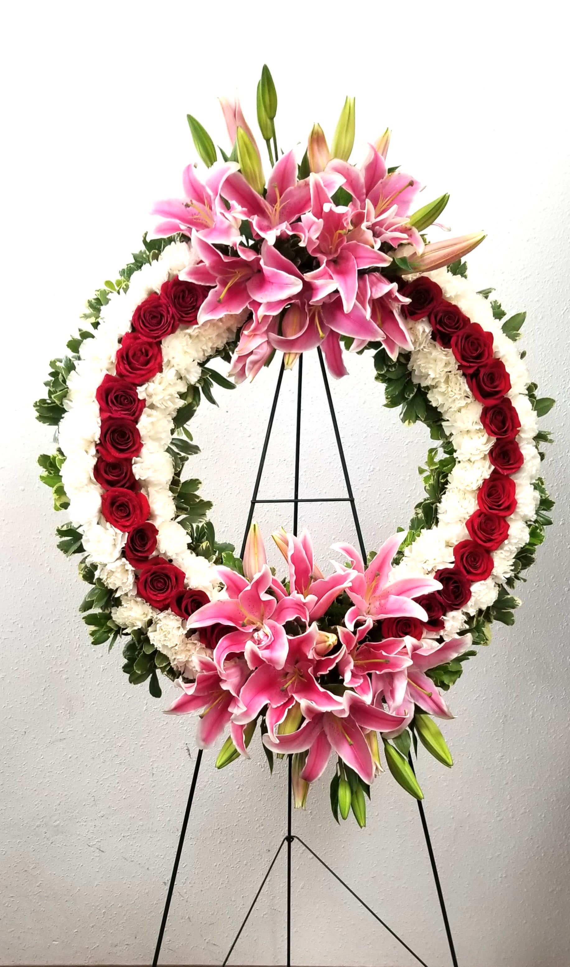 Standing floral wreath with pink lilies, red roses, and white flowers on an easel