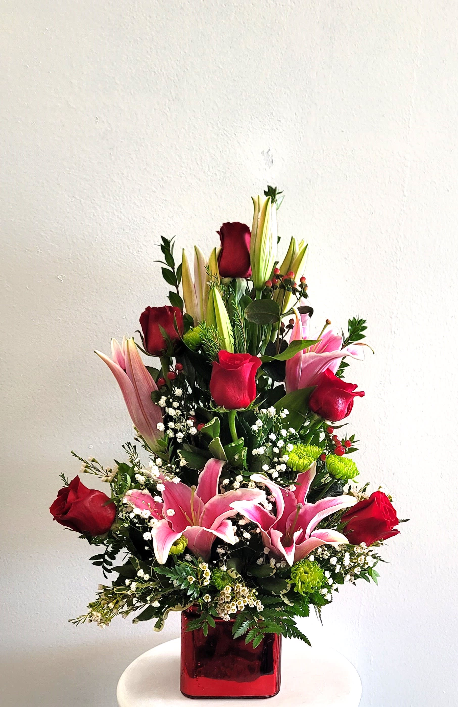 Tall bouquet of red roses and pink lilies in a red glass vase