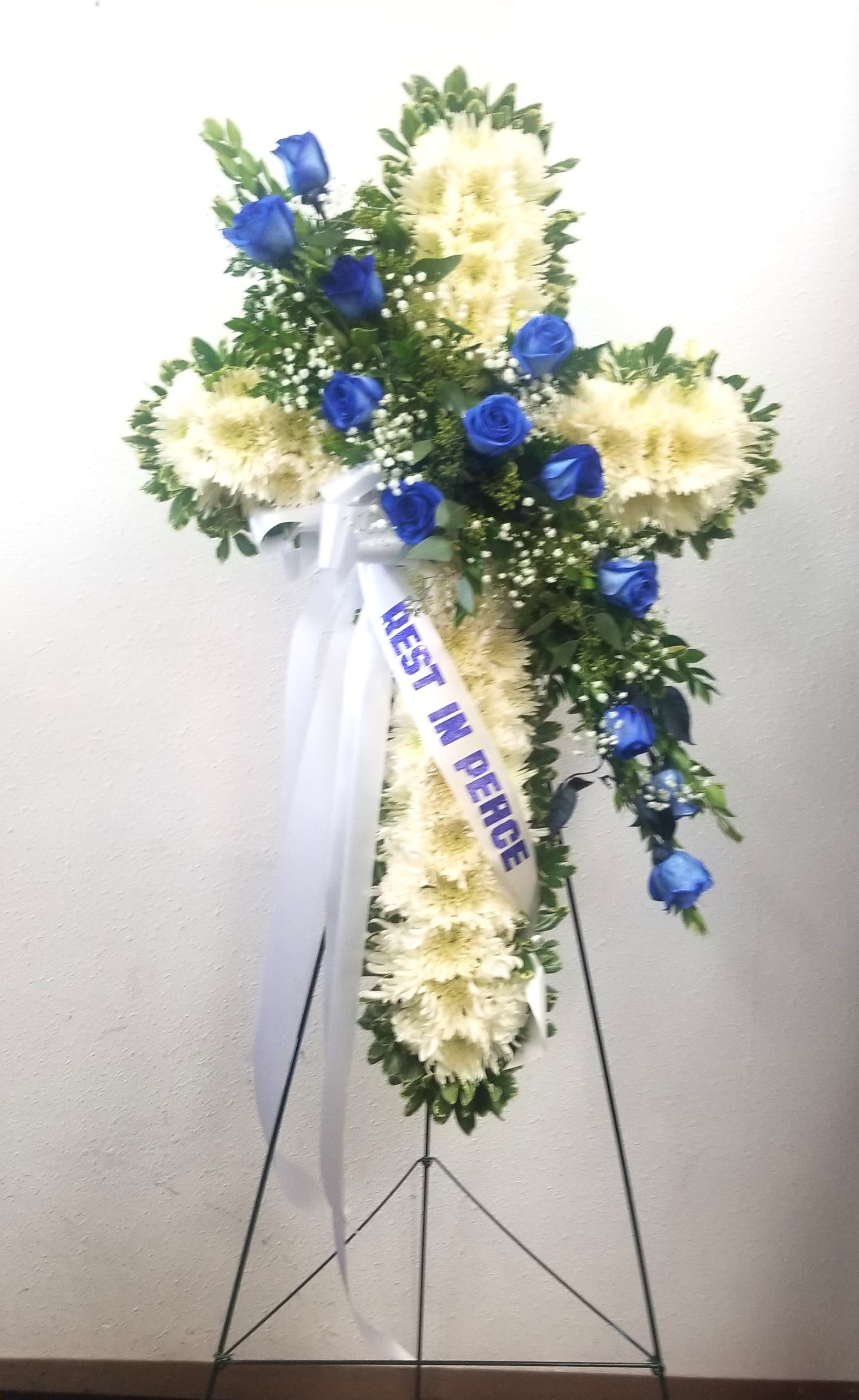 Standing floral cross with blue roses and white flowers on an easel