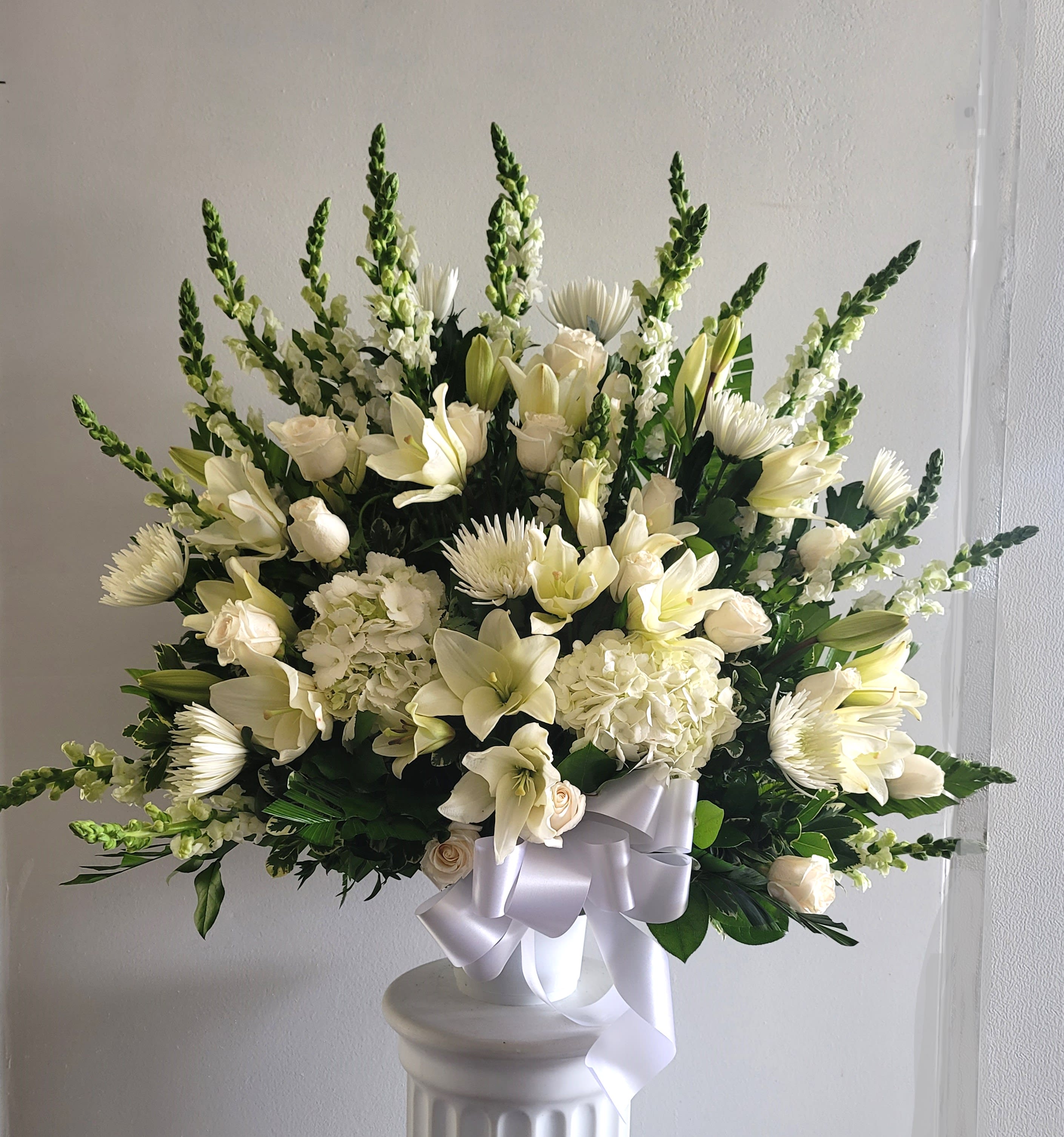 White floral arrangement with lilies, roses, and chrysanthemums in a pedestal vase