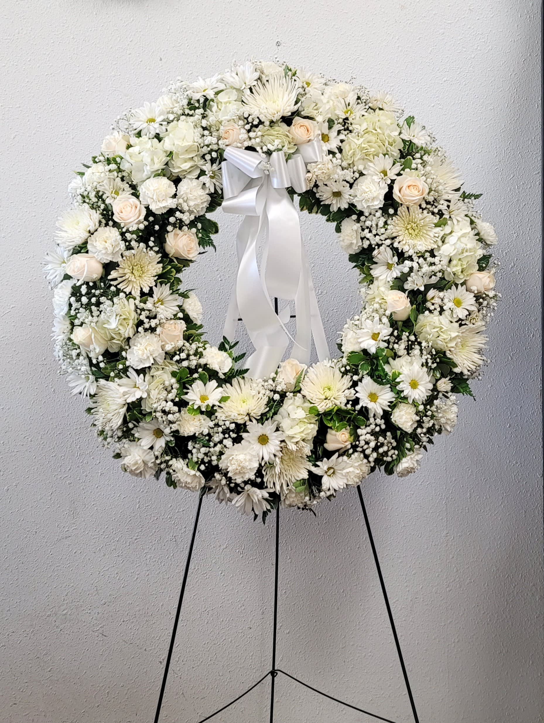 White floral wreath with a ribbon bow on a stand