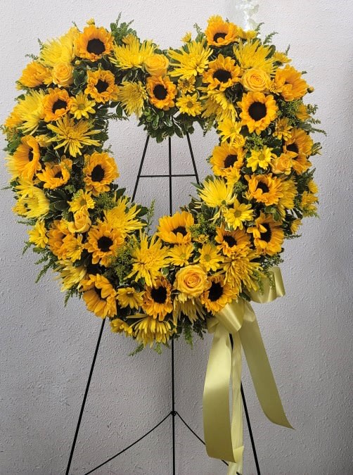 Heart-shaped yellow floral wreath on a stand with a ribbon