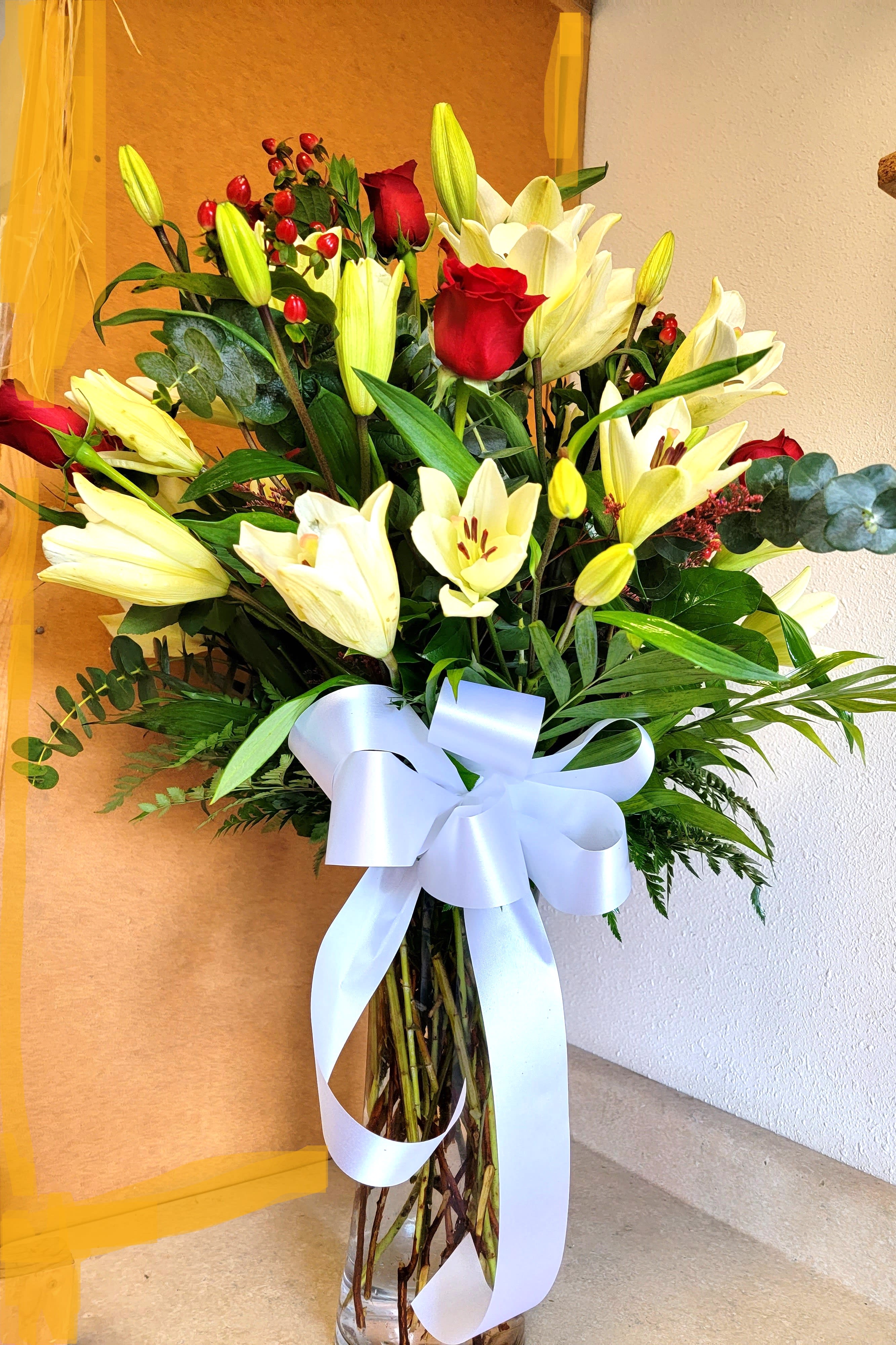 Tall bouquet of white lilies and red roses in a glass vase with a white ribbon