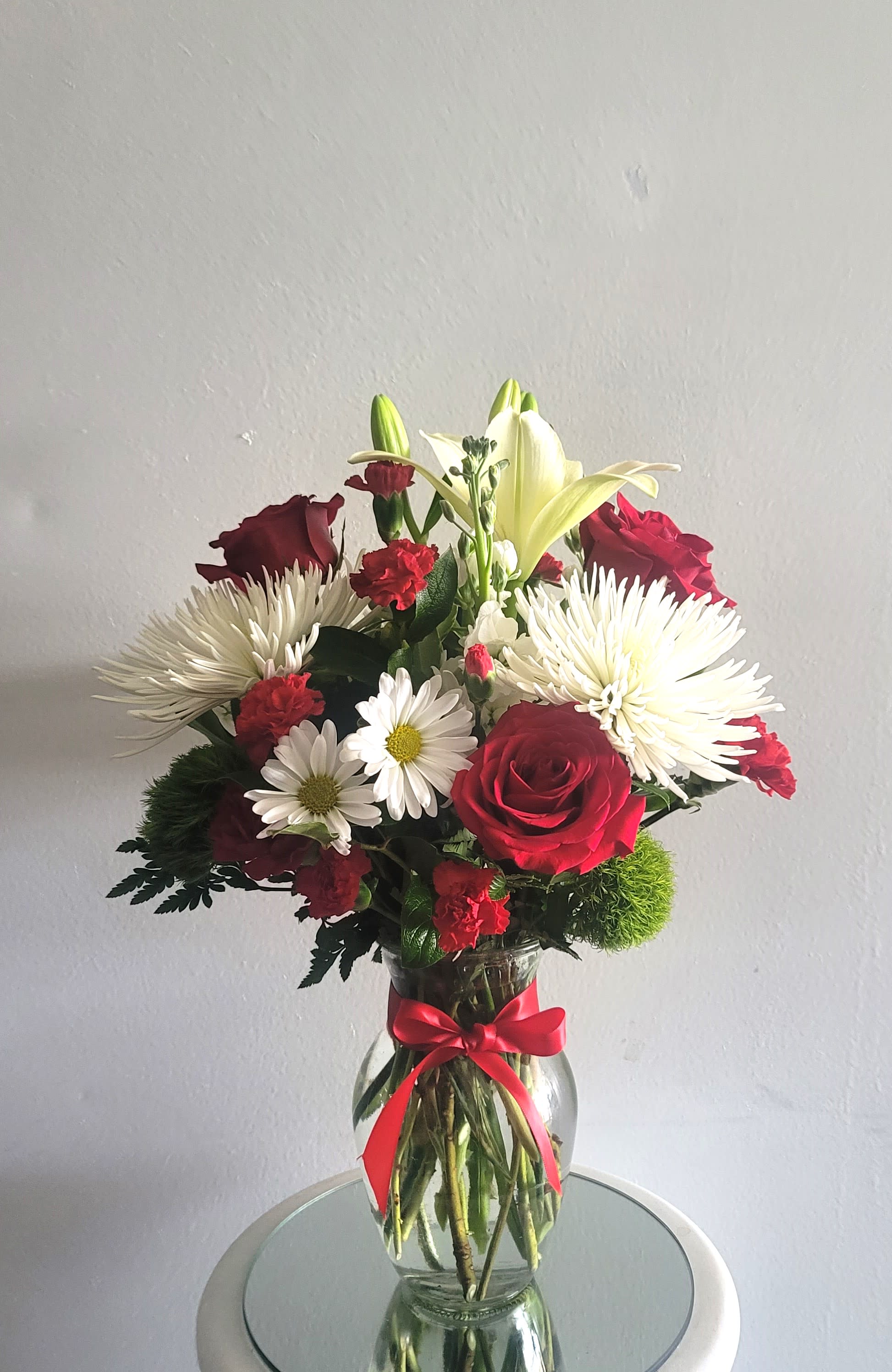 Bouquet of red roses, white lilies, and white daisies in a glass vase