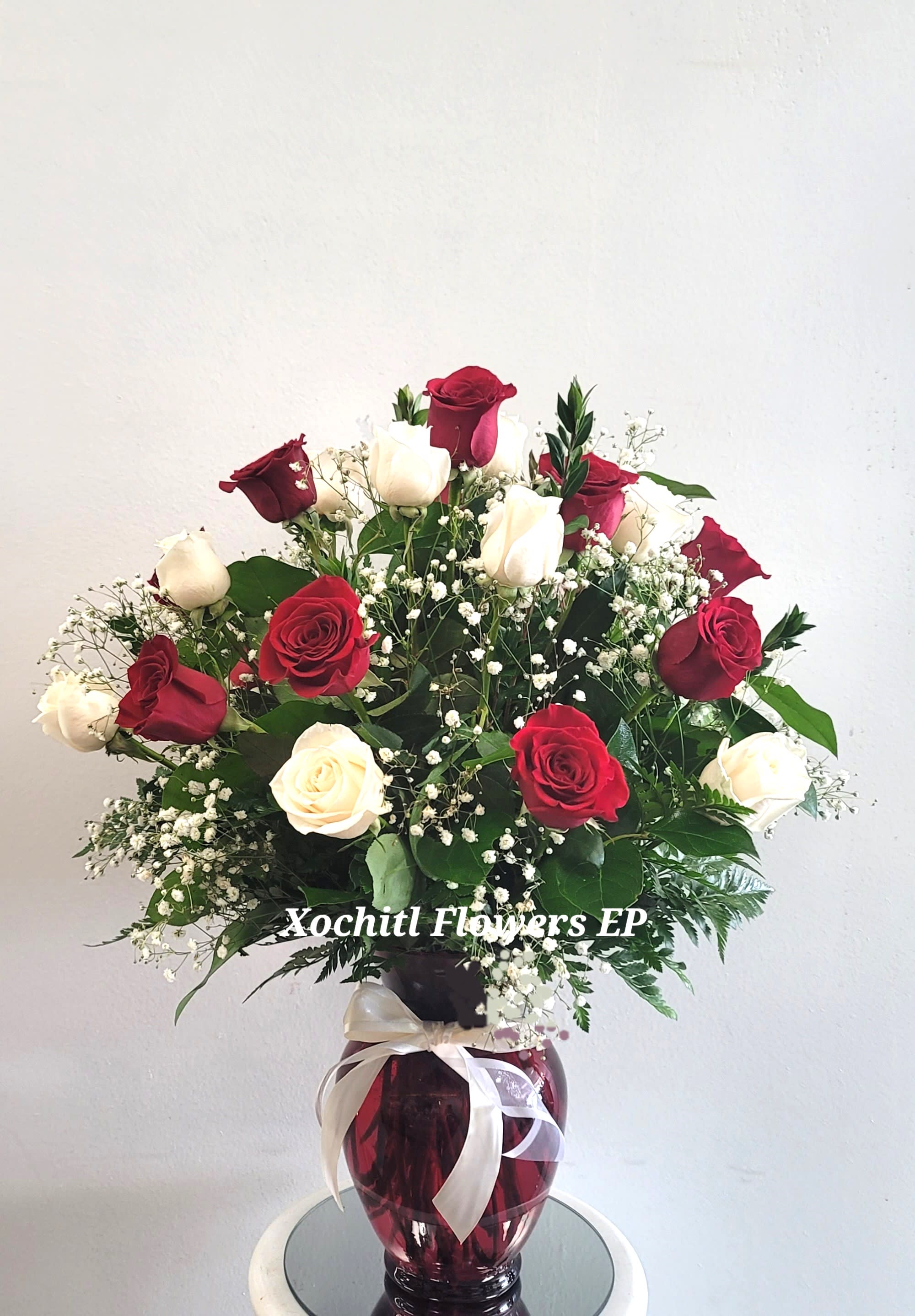 Red and white roses arranged in a burgundy vase with baby's breath