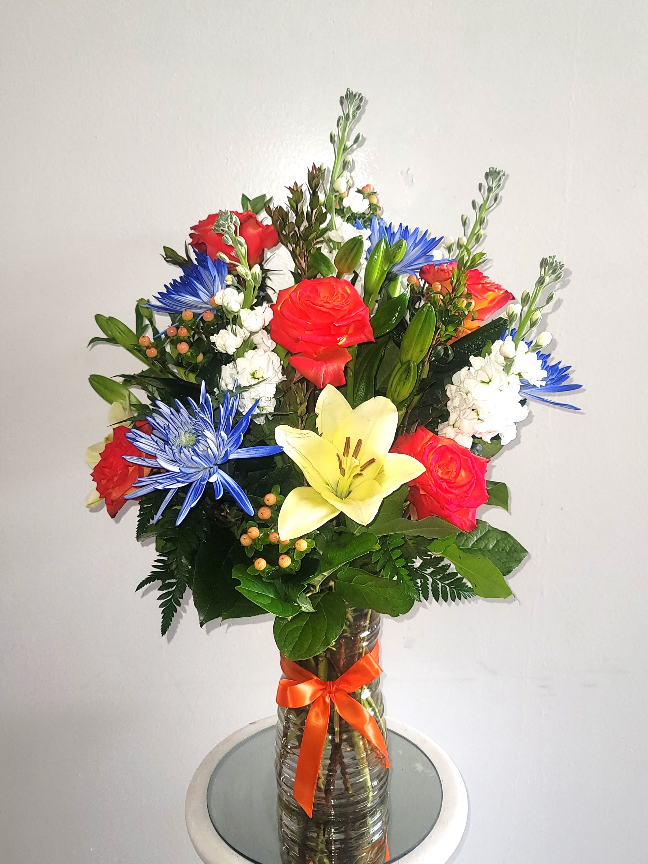 Mixed bouquet of roses, lilies, and blue daisies in a glass vase