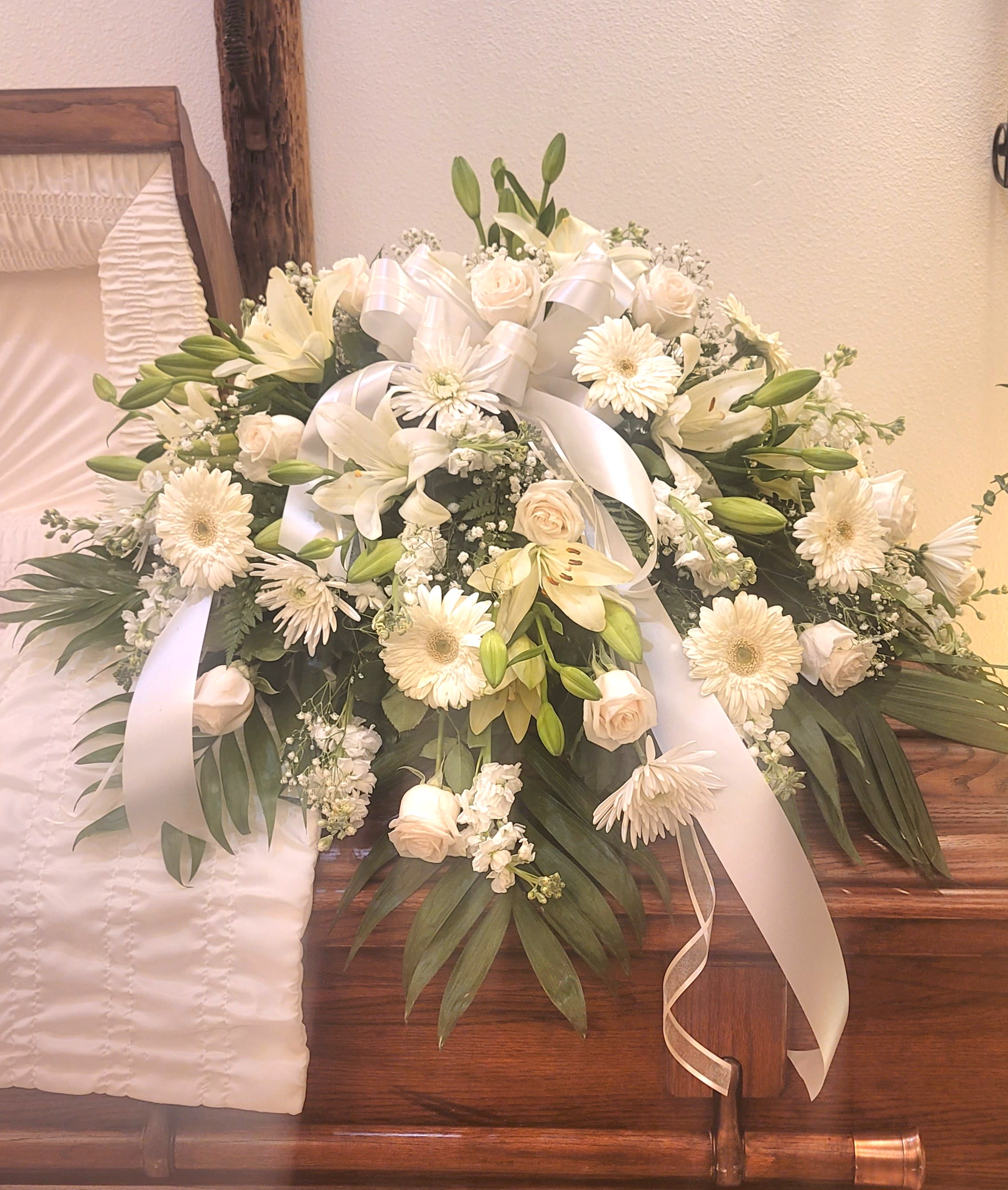 White floral casket spray with lilies, roses, and ribbon