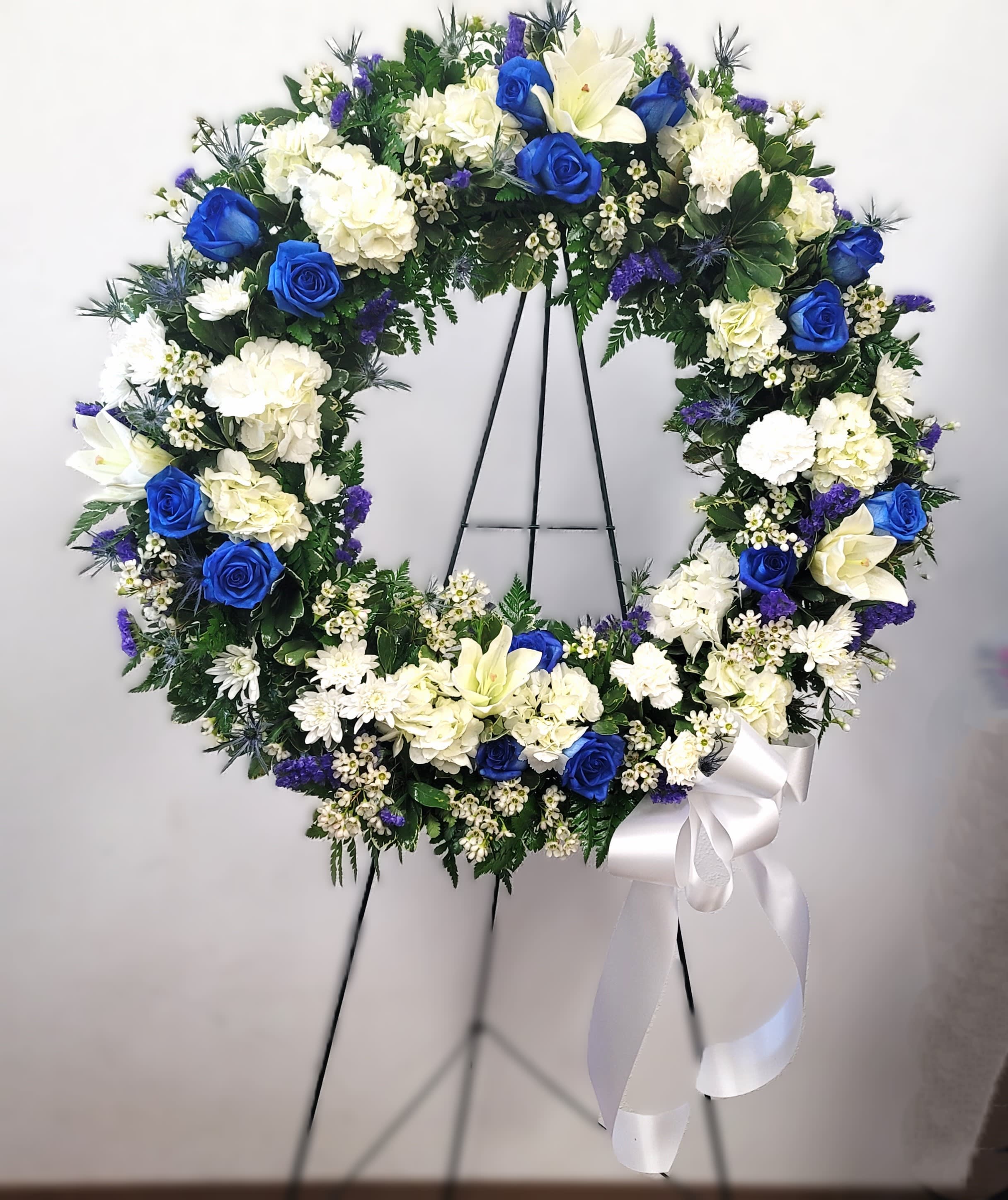 Blue and white floral wreath on a black stand with a white ribbon