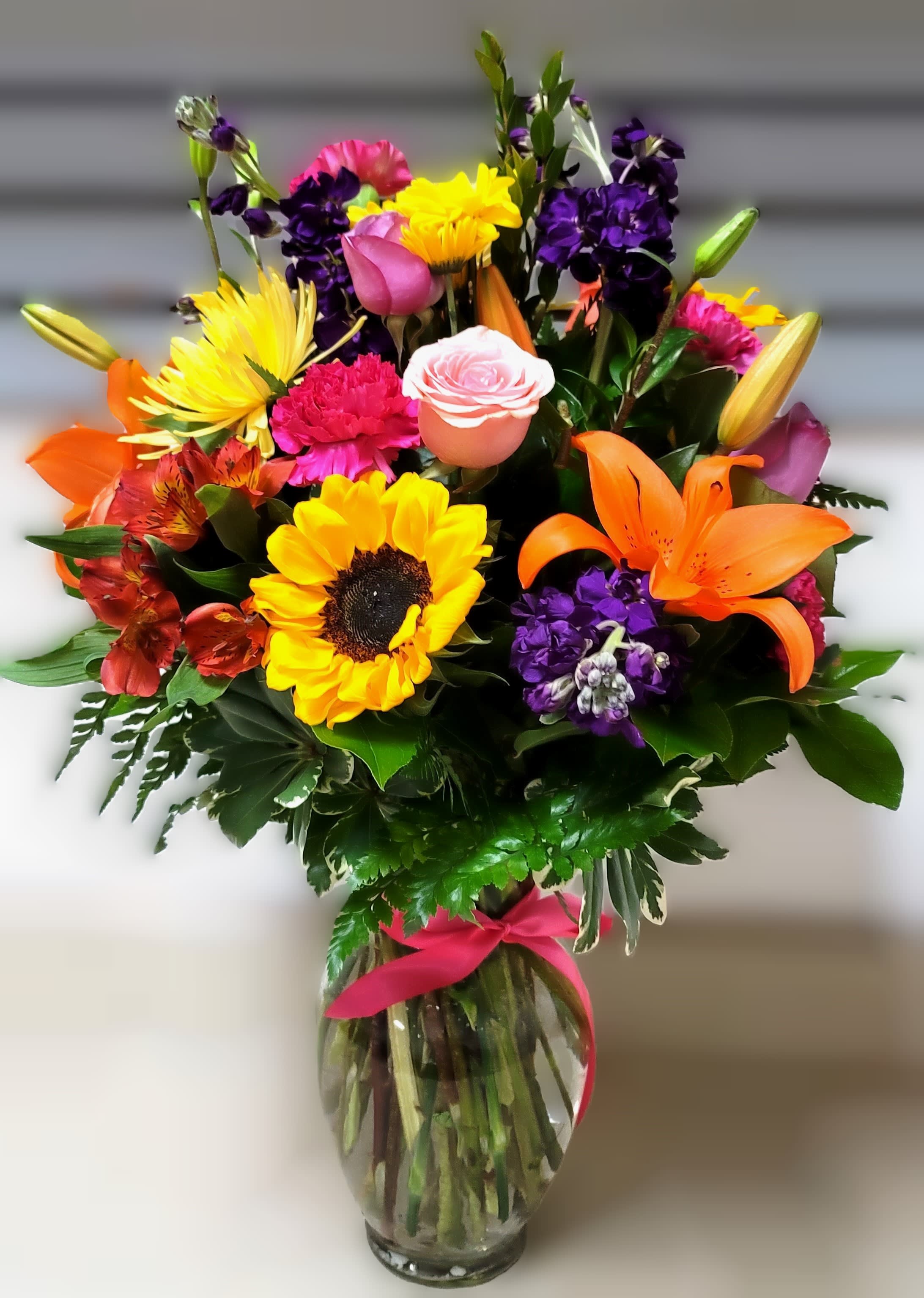 Colorful mixed bouquet in a glass vase with a pink ribbon