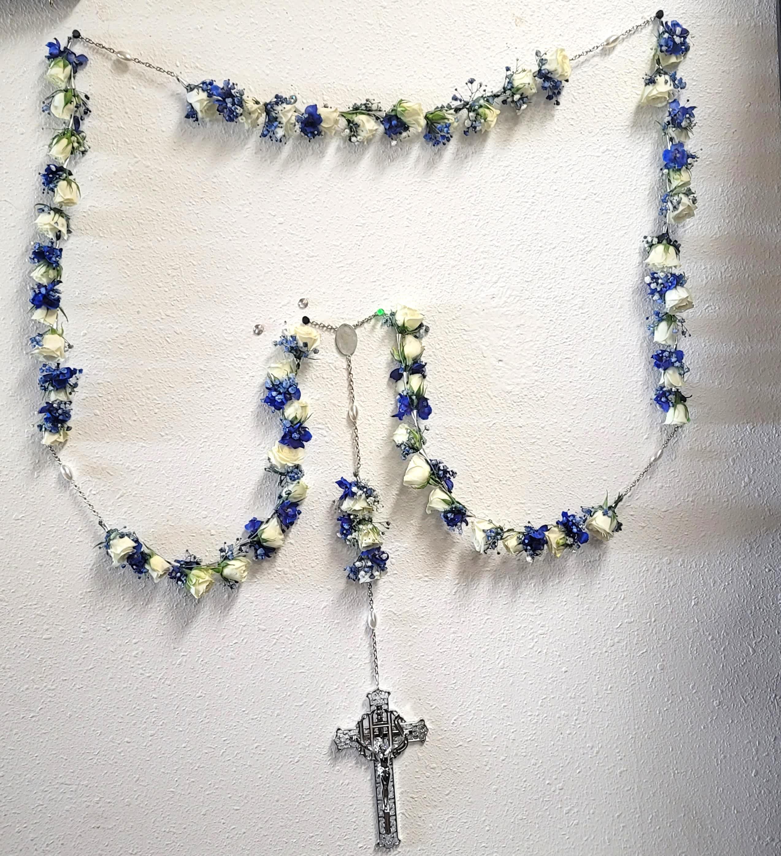 Blue and white floral garland arranged in a rosary shape with a cross pendant