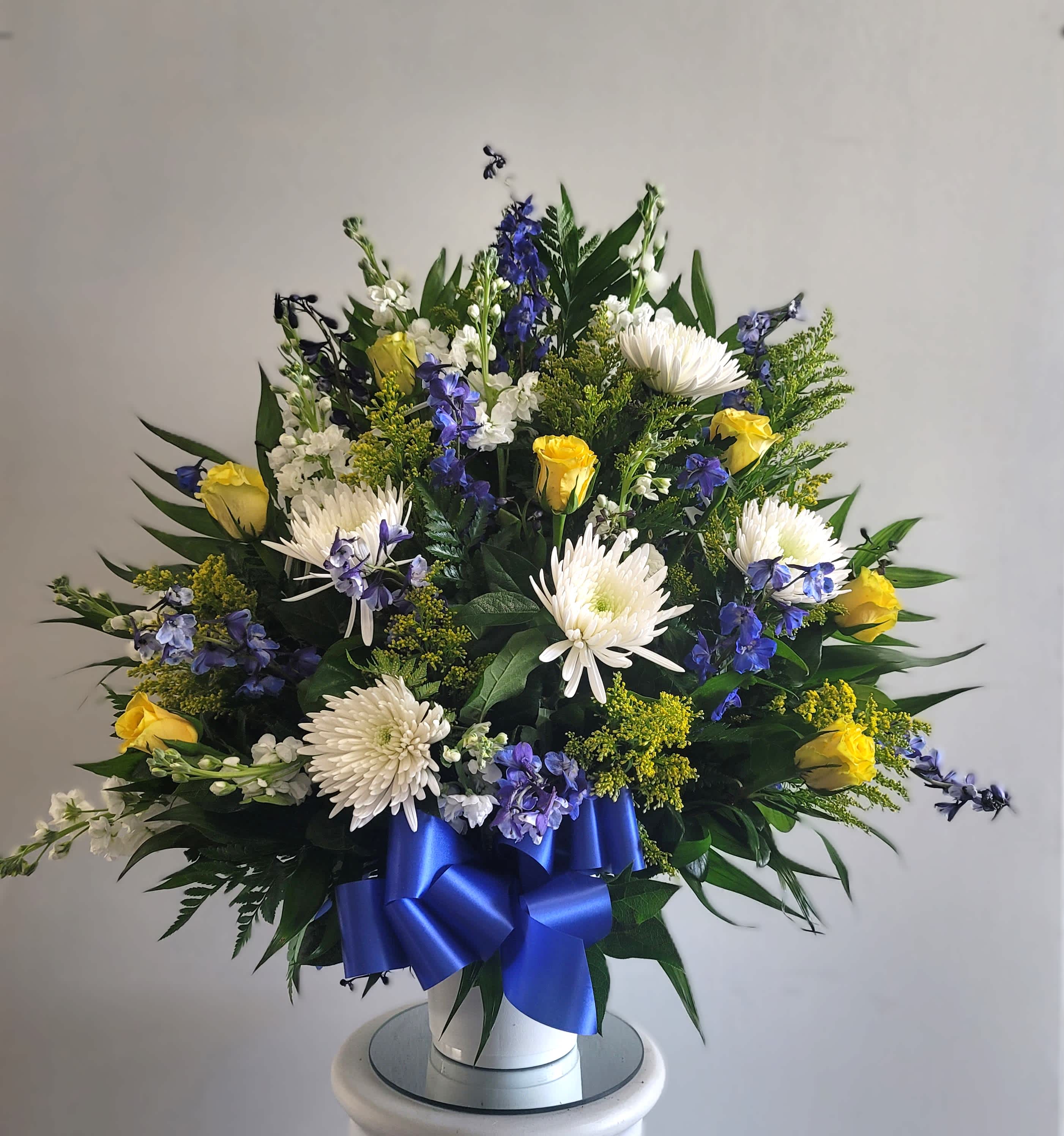 White and yellow floral arrangement with blue ribbon in a white vase