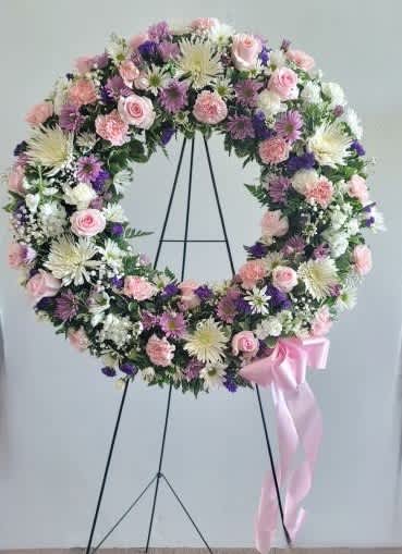 Pastel floral wreath on a black stand with a pink ribbon