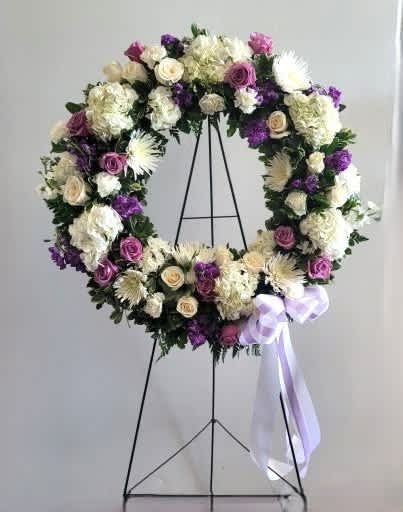 Circular floral wreath on a stand with purple, white, and cream flowers