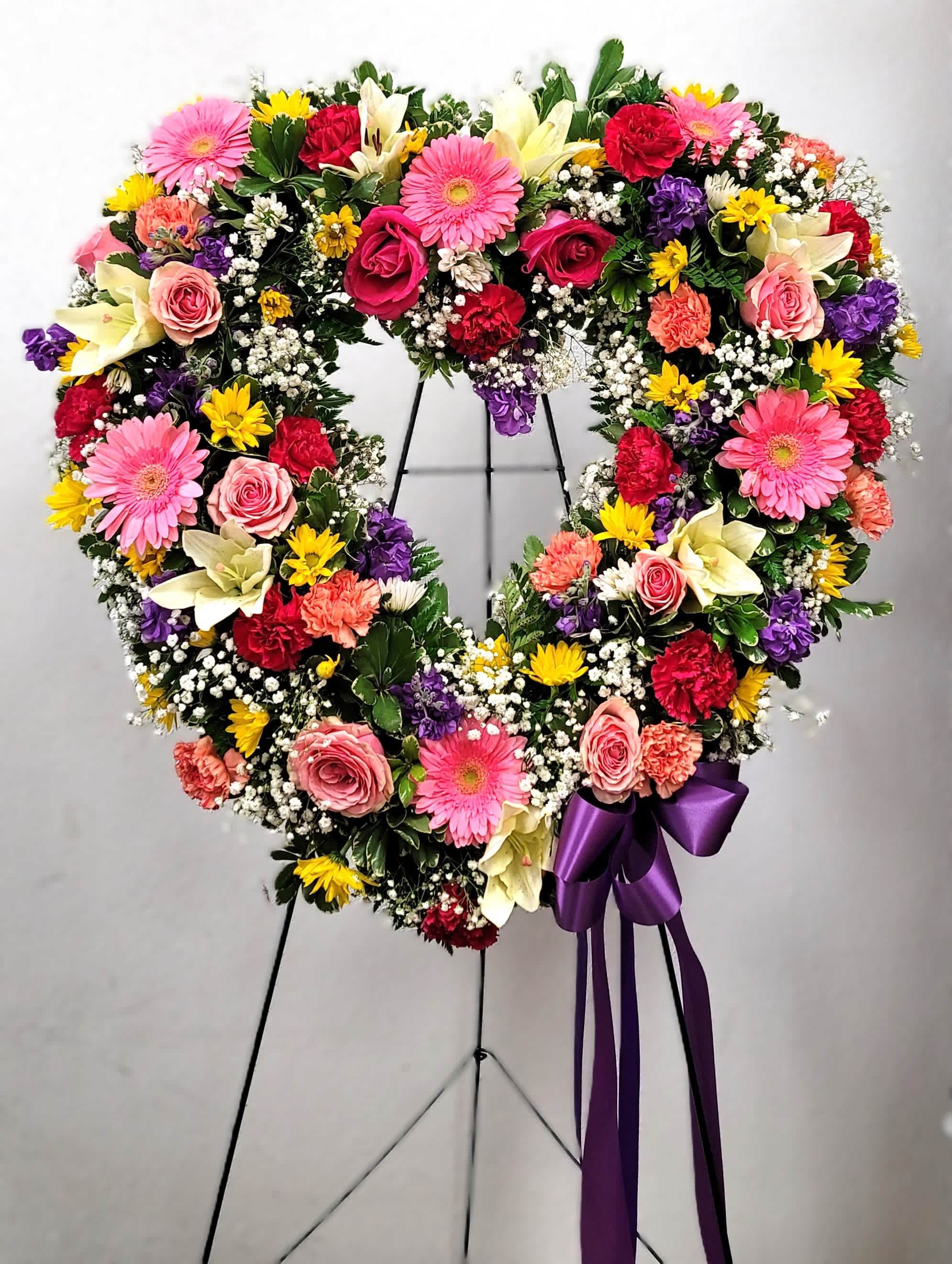 Heart-shaped floral wreath with pink, red, yellow, and white flowers on a stand