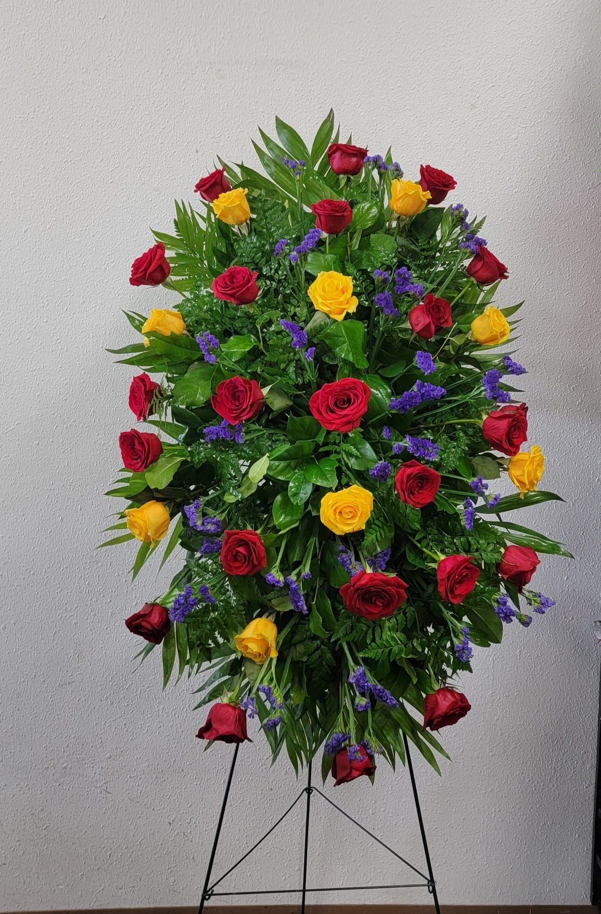 Large standing arrangement of red and yellow roses with purple filler flowers