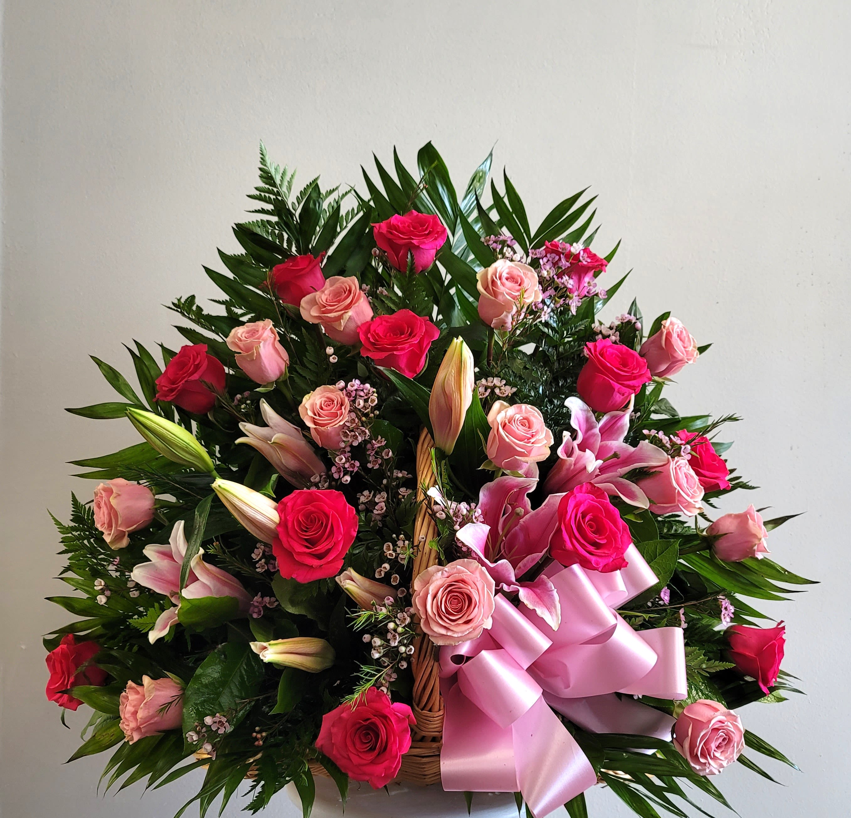 Basket arrangement of pink and red roses with lilies and a pink ribbon