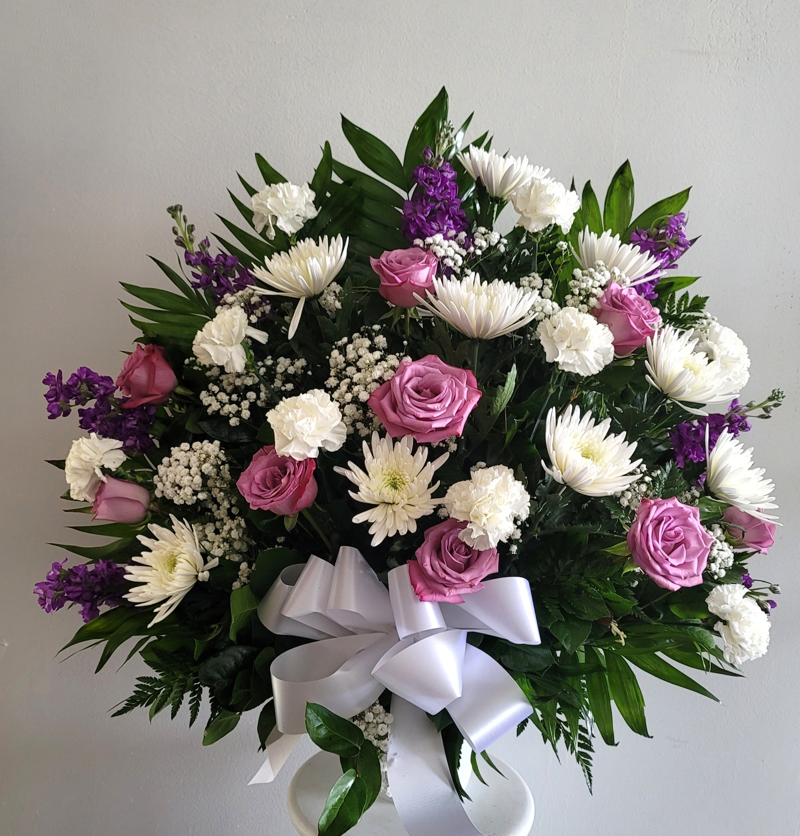 Bouquet of pink roses, white daisies, and purple flowers with a white ribbon