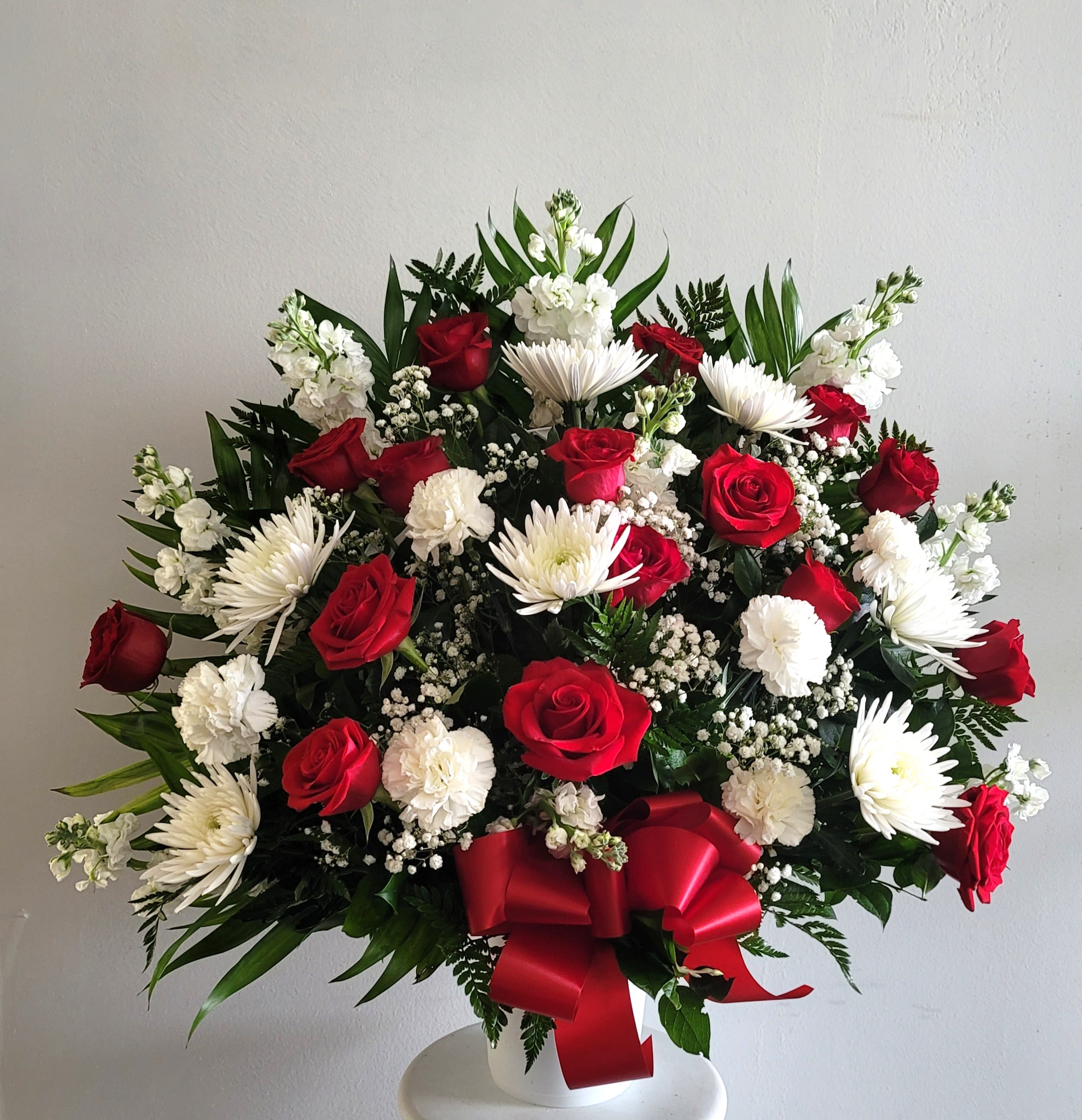Red roses and white daisies in a white vase with a red ribbon