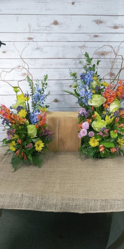 Two colorful floral arrangements flank a wooden box on burlap