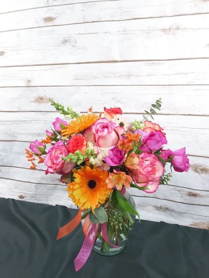 Colorful bouquet of pink roses and orange gerbera daisies in a glass vase