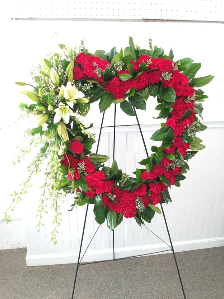 Heart-shaped floral wreath with red carnations and white lilies on a stand