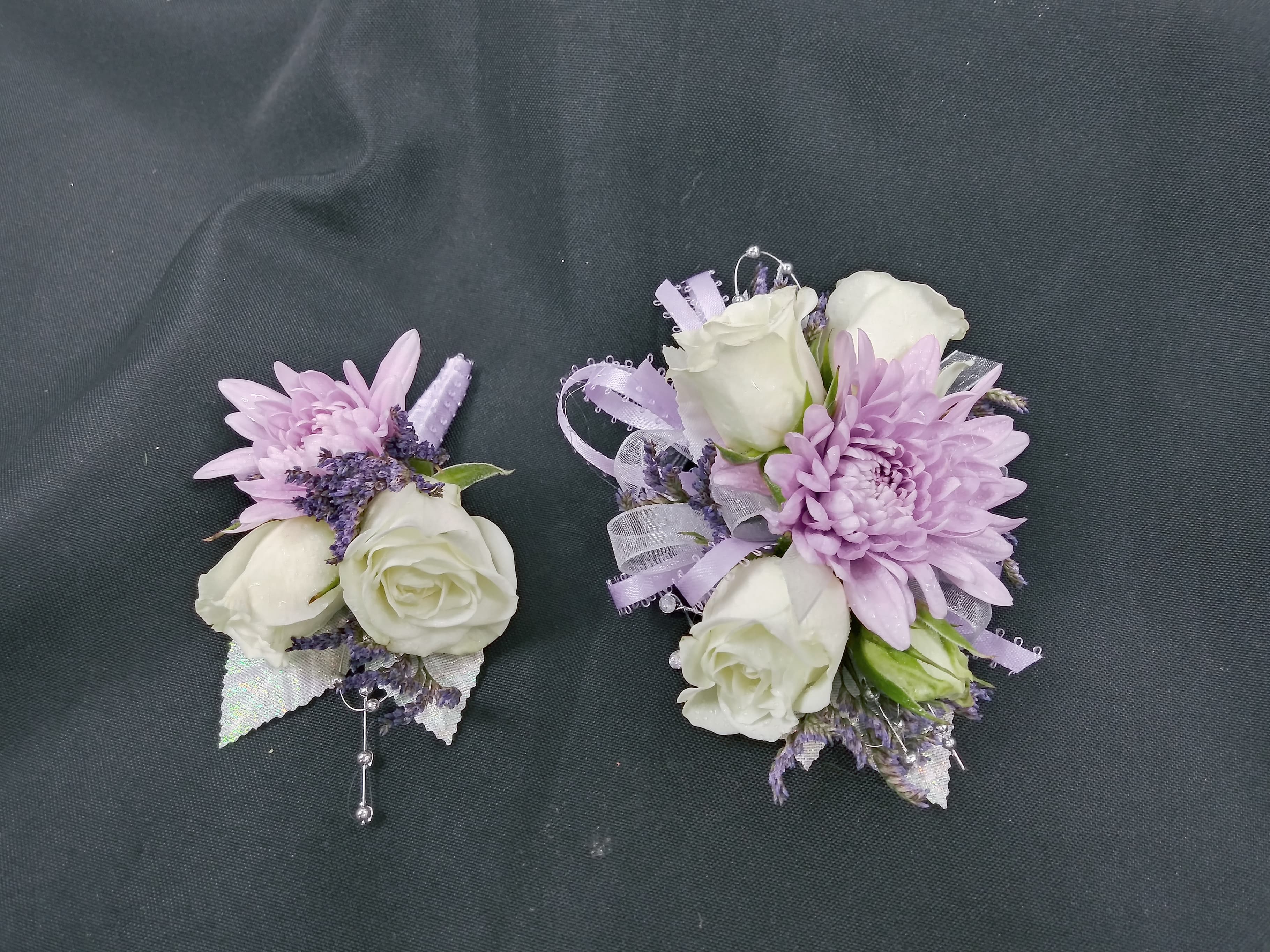 Two lavender and white floral corsages on a dark fabric background