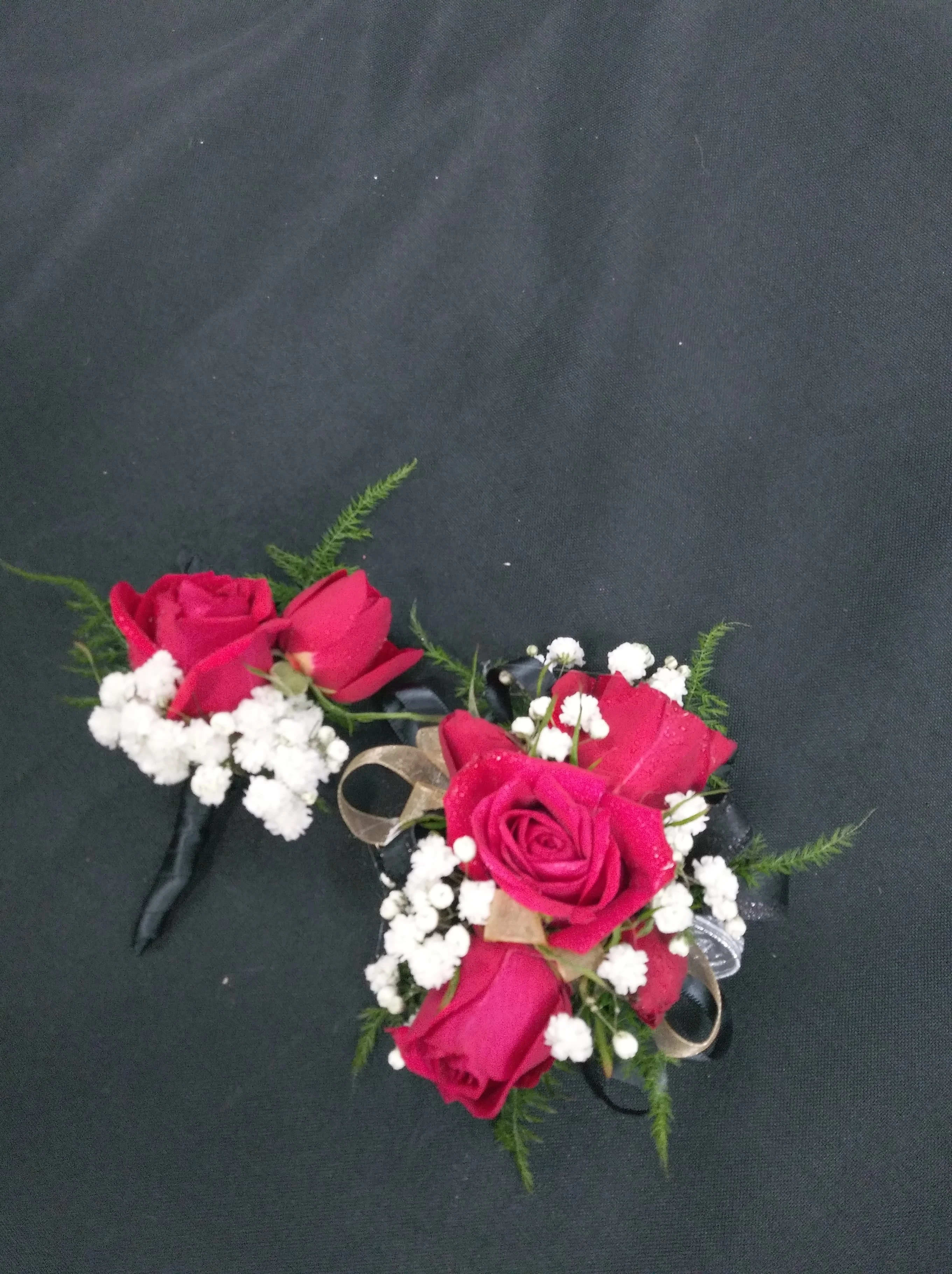 Two red rose corsages with white baby's breath on black ribbon