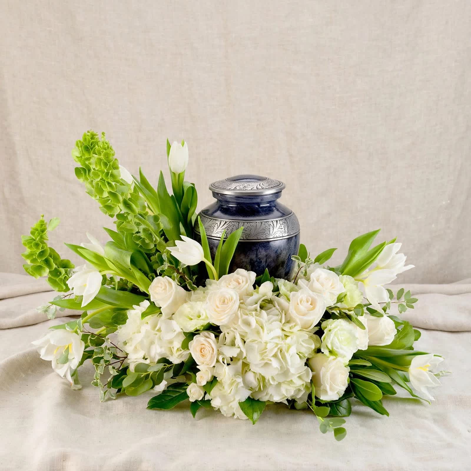 White floral arrangement with roses and tulips around a dark blue urn