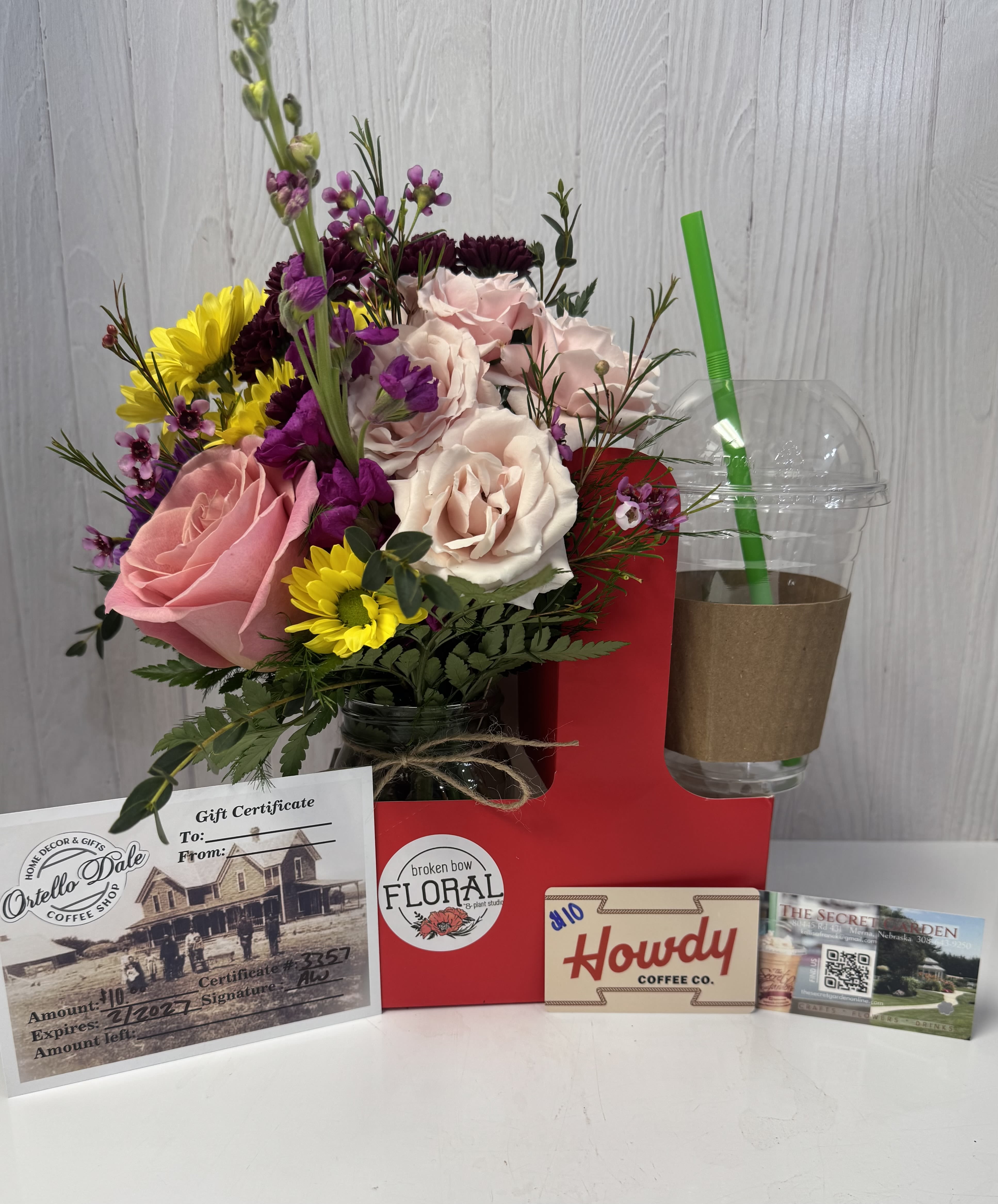 Mixed bouquet with pink and white roses in a jar, beside gift cards and a drink cup.