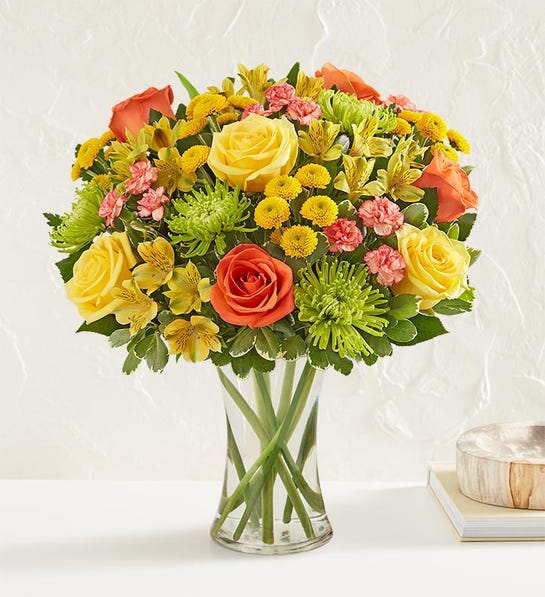 Mixed bouquet of yellow, orange, and pink flowers in a clear glass vase