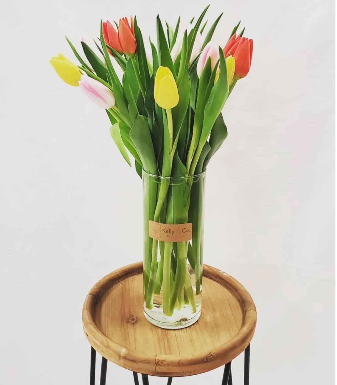 Glass vase of colorful tulips on a wooden stand