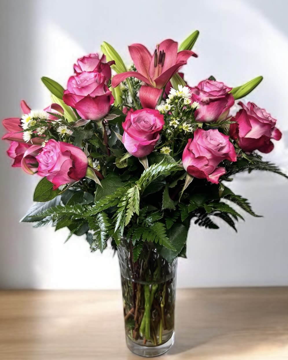 Pink roses and a lily arranged in a clear glass vase