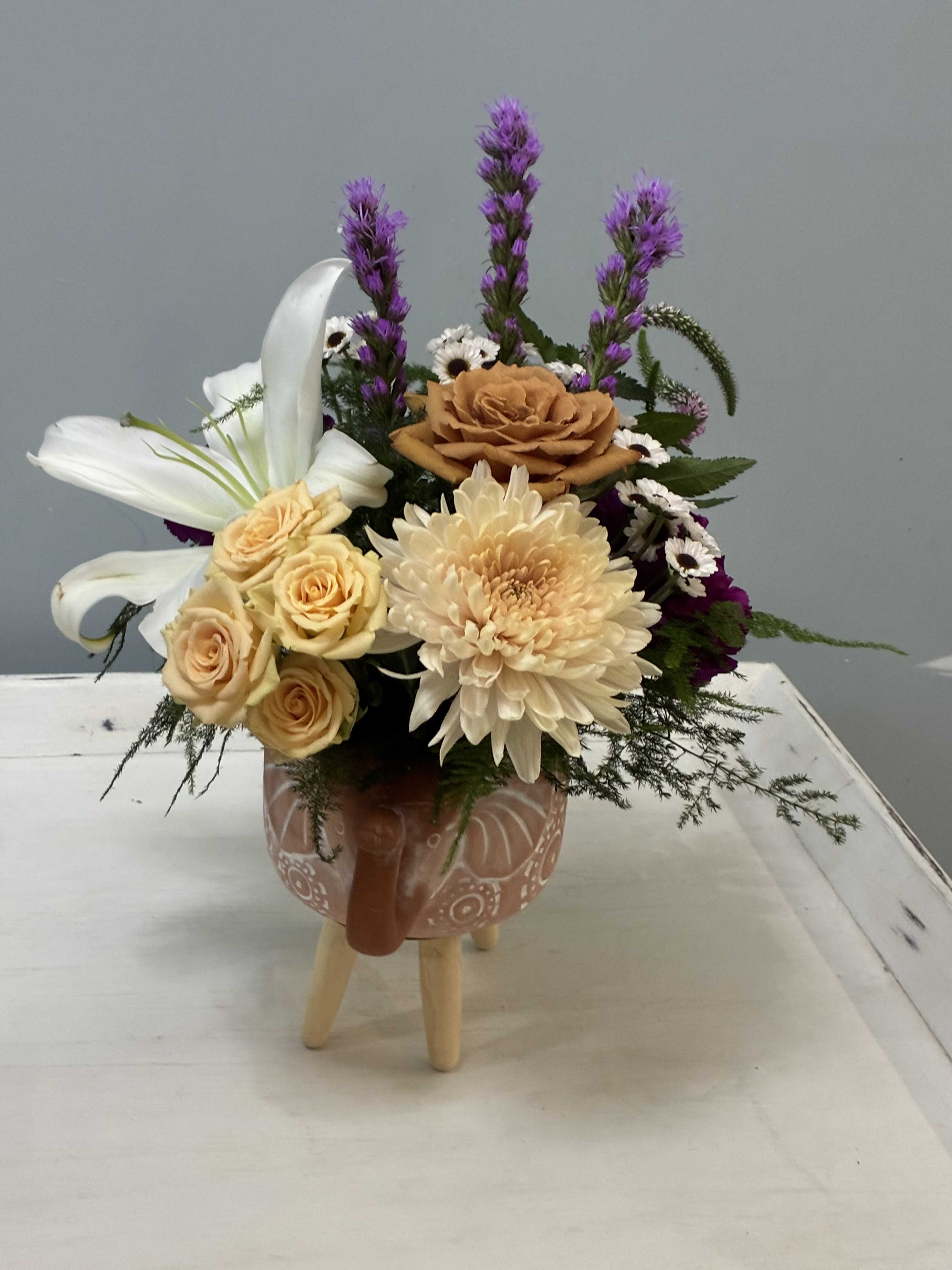 Mixed flower arrangement in a patterned ceramic mug on a small stand