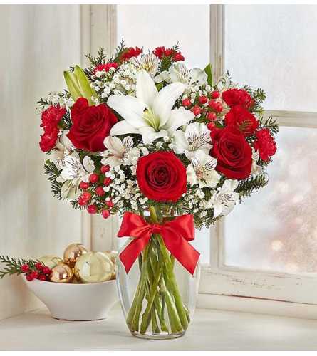 Red roses and white lilies in a clear glass vase with a red ribbon