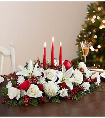 Holiday centerpiece with white flowers, red candles, and pinecones on a table