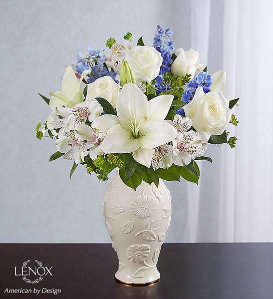White lilies and roses arranged in a decorative vase with blue accents