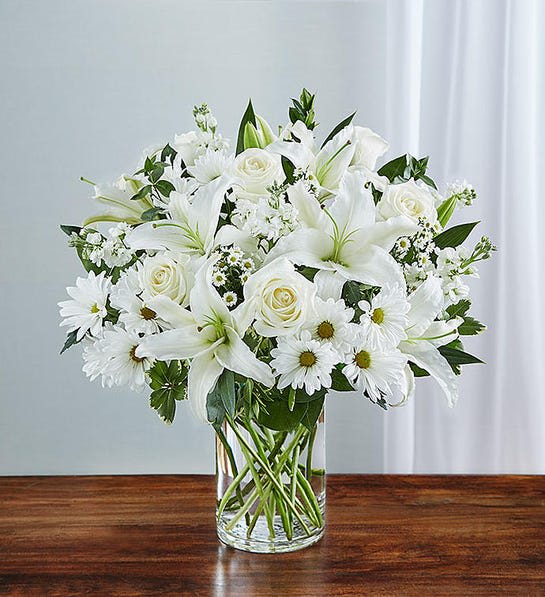 White lilies, roses, and daisies arranged in a clear glass vase