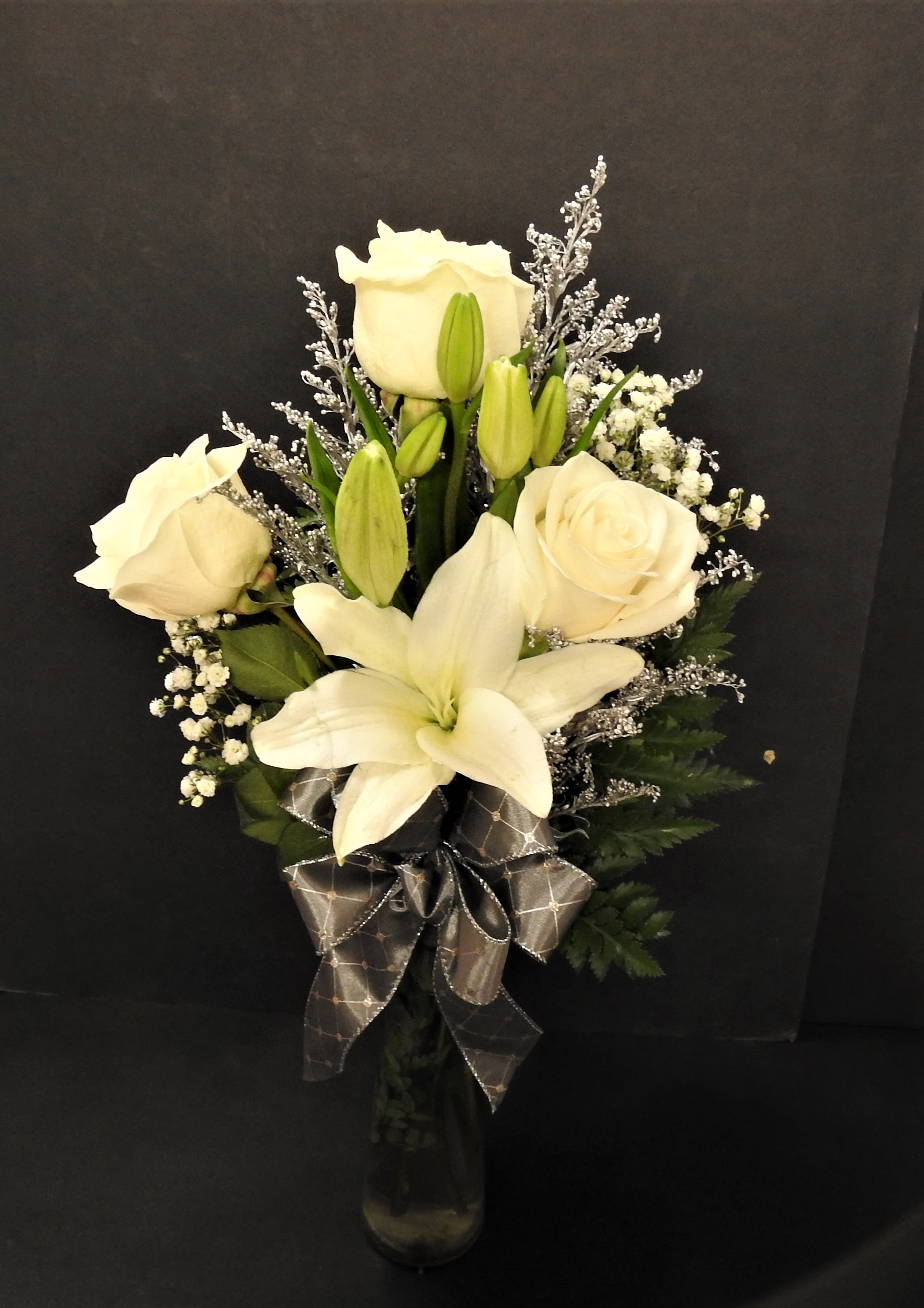 White roses and lilies arranged in a glass vase with a dark ribbon