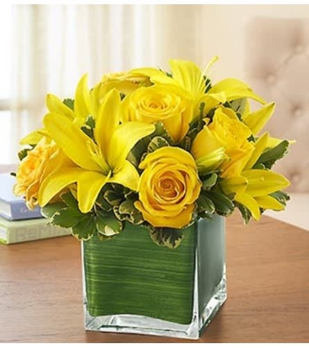 Yellow roses and lilies arranged in a square glass vase