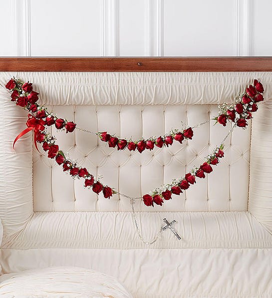 Red rose garlands draped across a white upholstered headboard with a small cross pendant