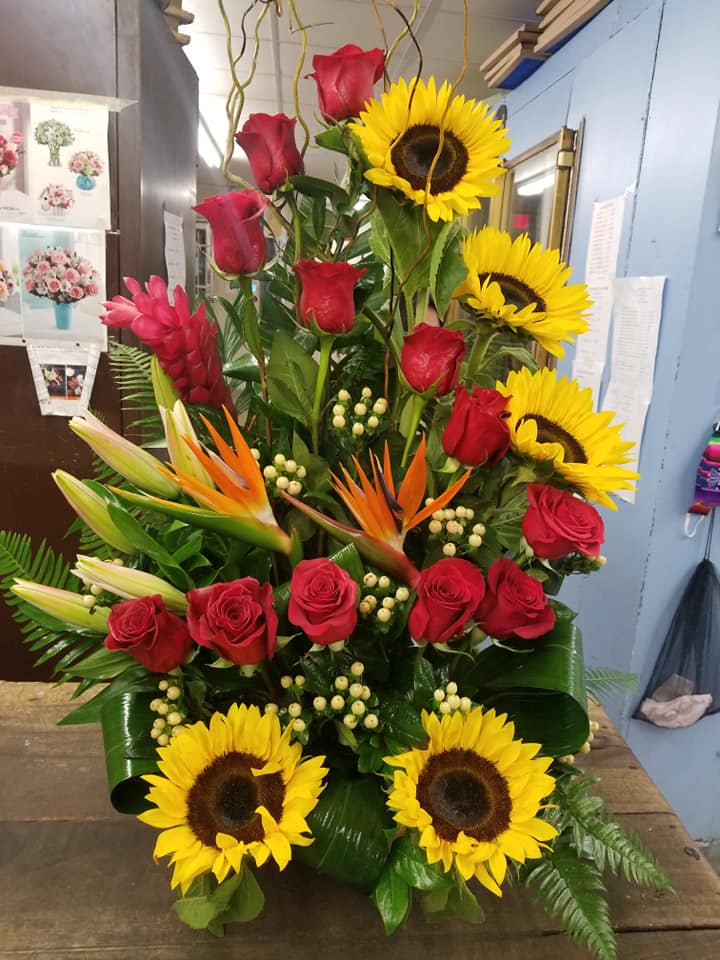 Tall arrangement of red roses, sunflowers, and tropical blooms
