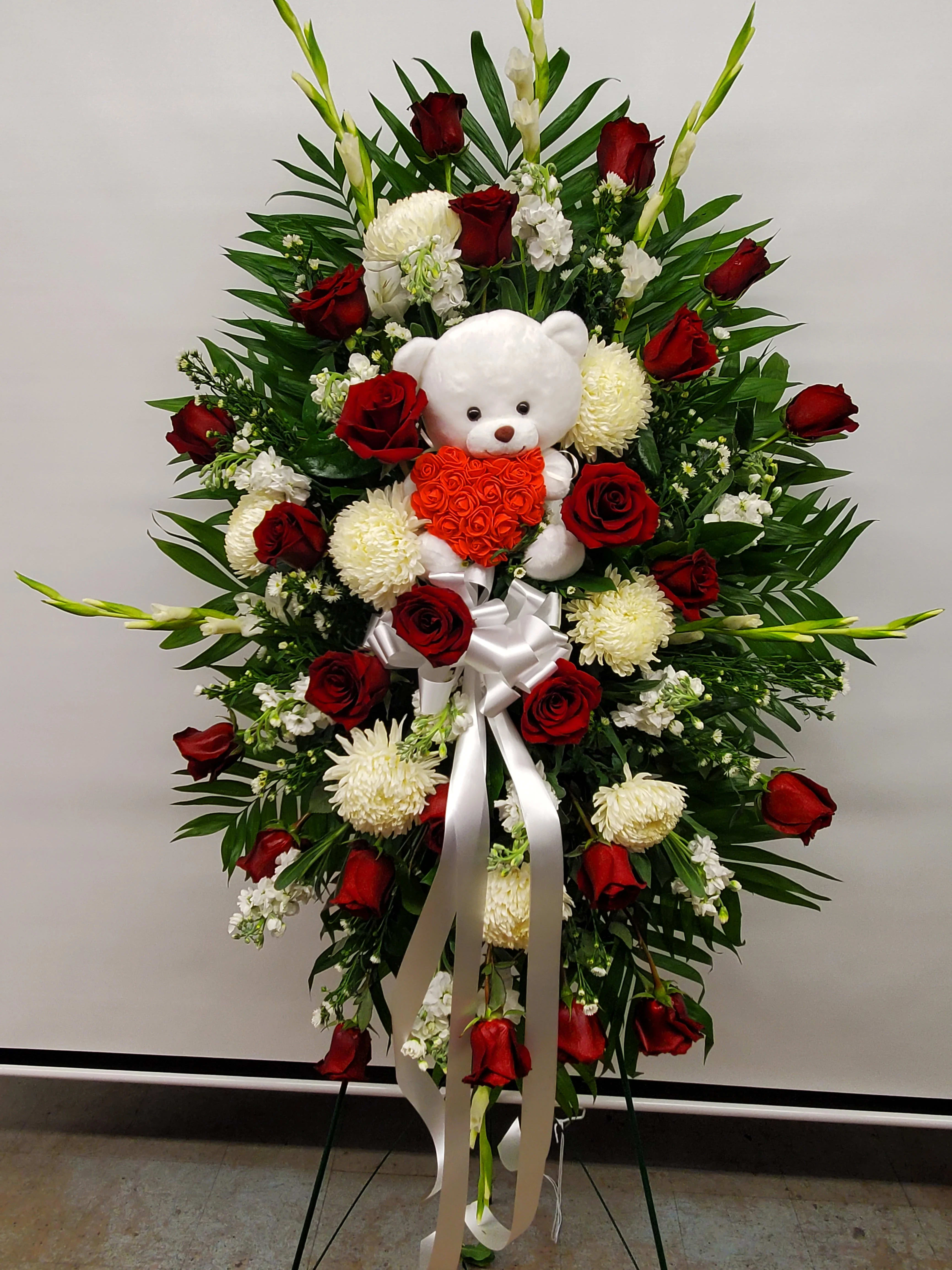 Standing floral spray with red roses, white blooms, and a teddy bear centerpiece
