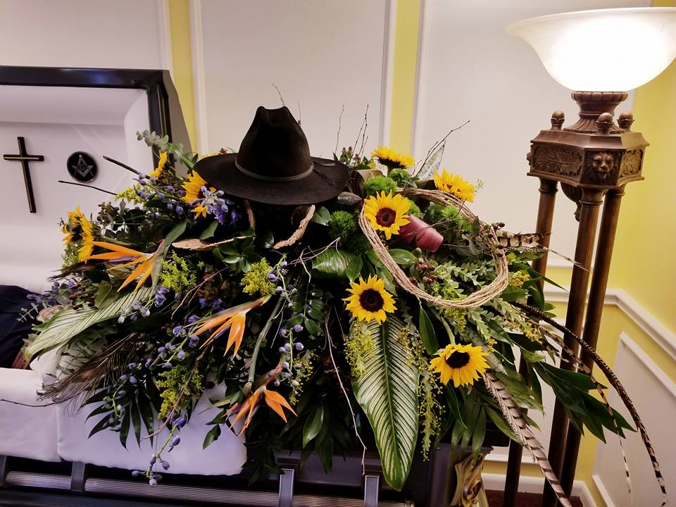 Large funeral casket spray with sunflowers and a black cowboy hat