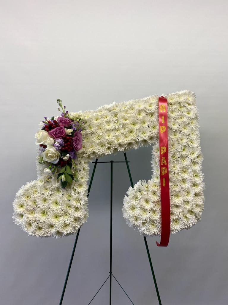 Large white floral funeral wreath on an easel with a red ribbon