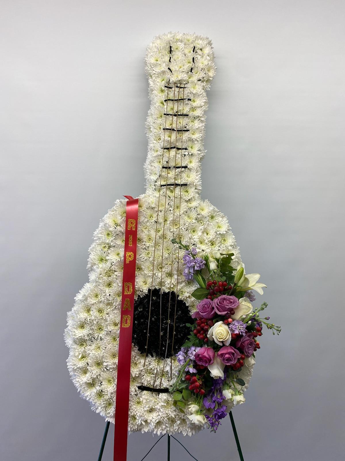 Standing guitar-shaped floral tribute with white flowers and a red ribbon