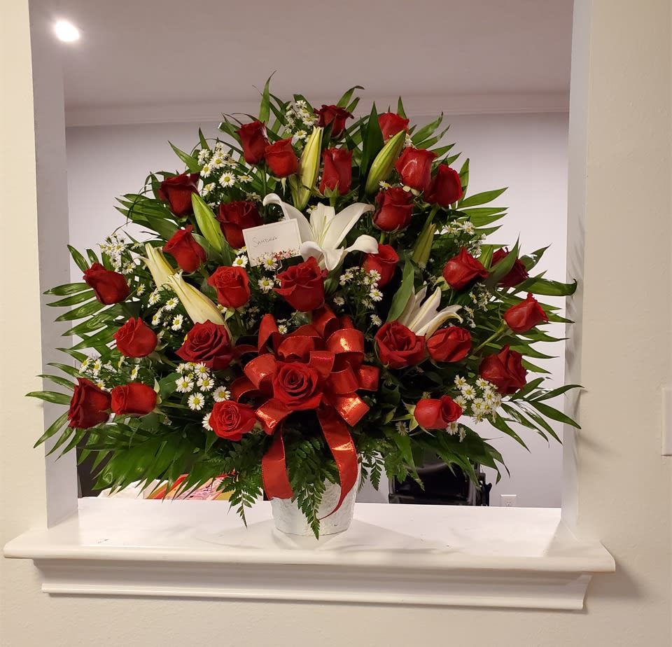 Large bouquet of red roses and white lilies in a white vase with a red ribbon