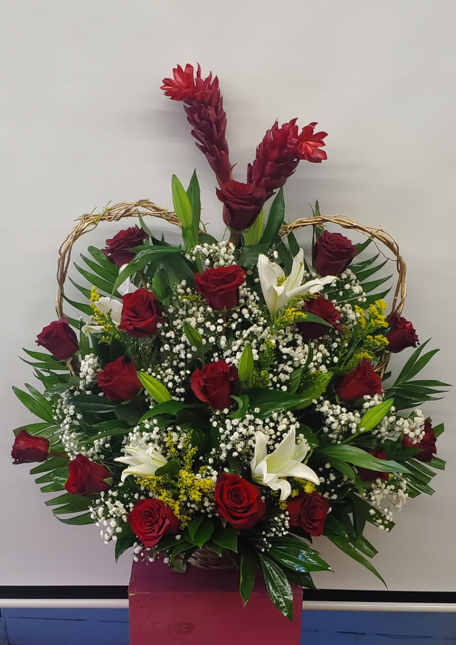 Basket arrangement of red roses, white lilies, and burgundy tropical blooms