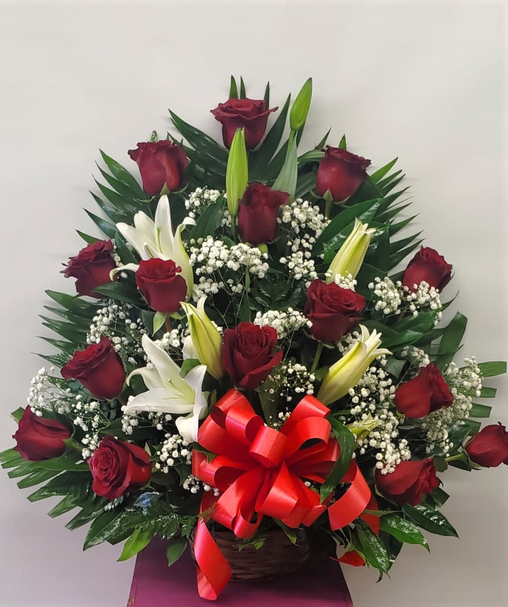 Basket arrangement of red roses and white lilies with a red bow