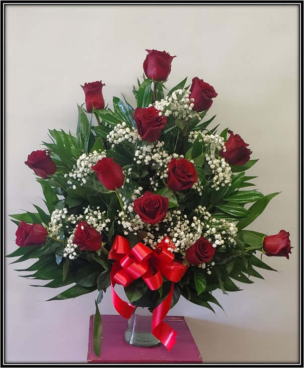 Red roses arranged in a clear vase with baby's breath and a red ribbon